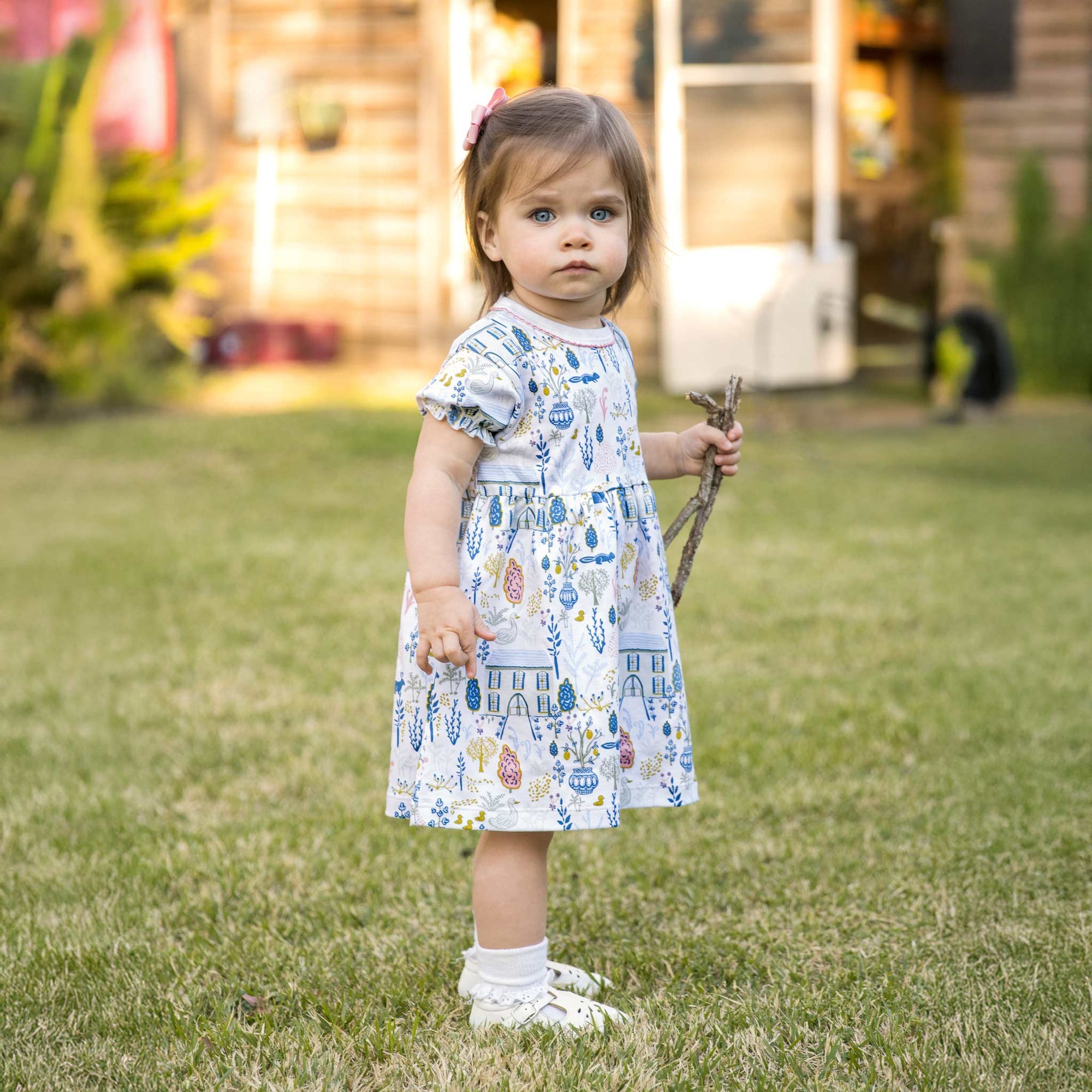 Adorable toddler in play dress in field with countryside print.