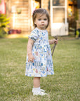 Adorable toddler in play dress in field with countryside print.