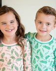 Children wearing Pink and Blue two-piece pajama sets with vintage Christmas holly pattern made with pima cotton