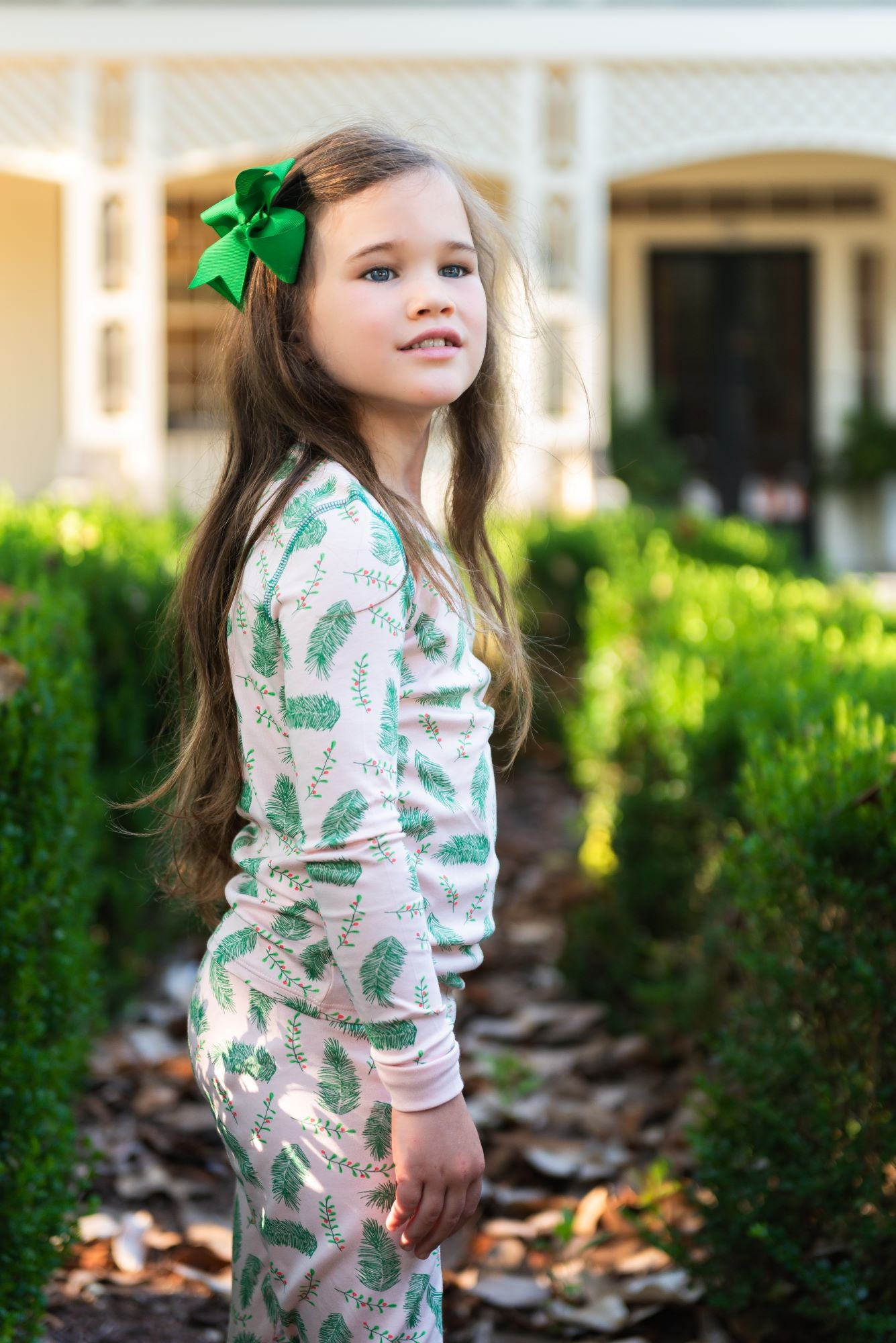 Little Girl wearing Pink two-piece pajama set with vintage Christmas holly pattern made with pima cotton