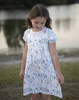 Young girl wearing Heyward House pima play dress with countryside print in mustard and blue colors.