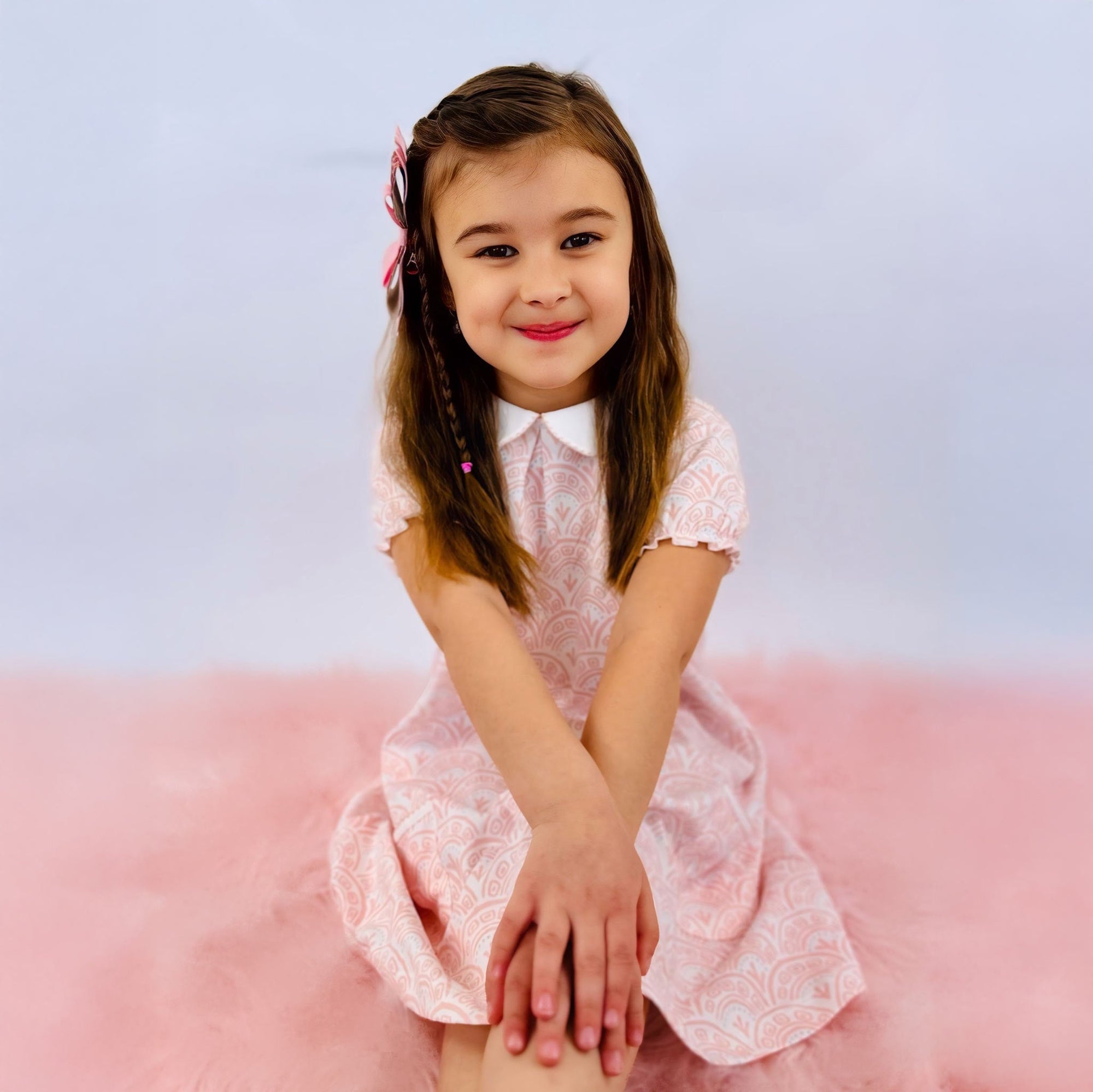 Young girl with hands on knees in Heyward House pocket twirl dress with delicate pink pattern.