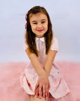Young girl with hands on knees in Heyward House pocket twirl dress with delicate pink pattern.