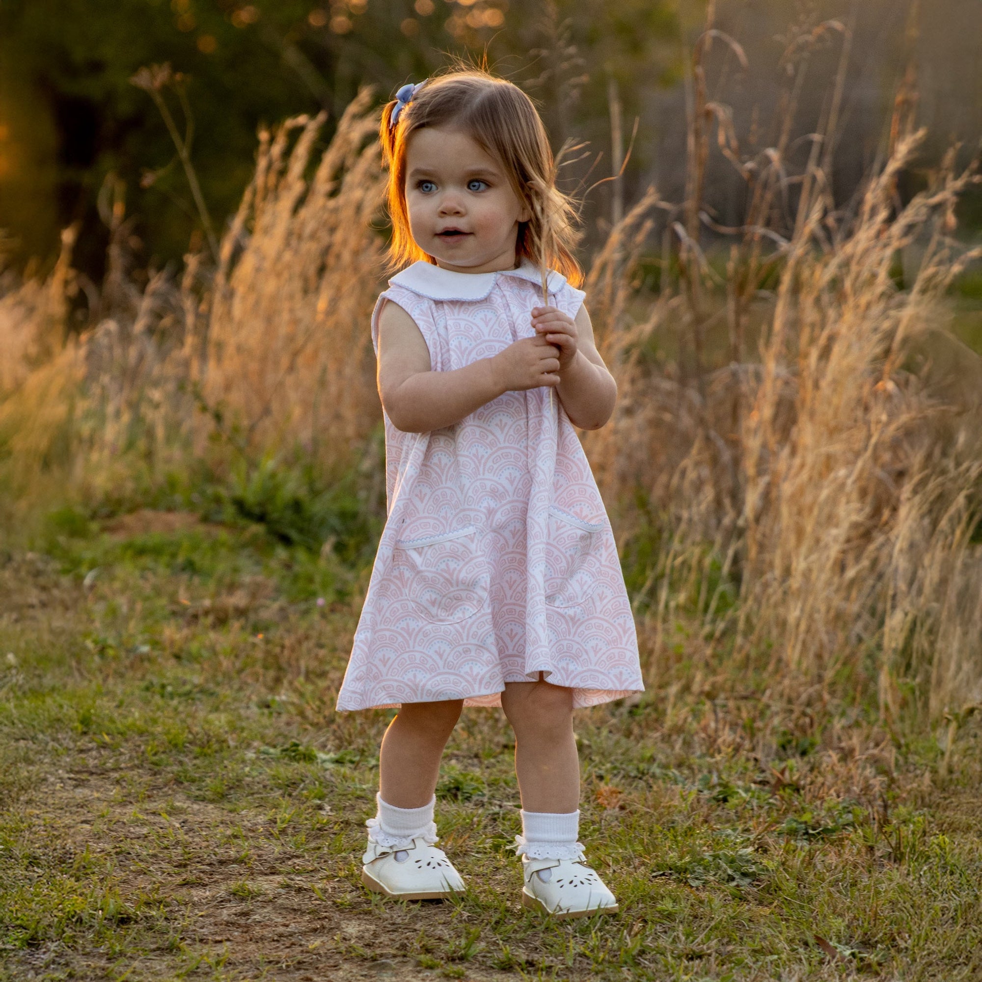 Toddler in Heyward House pima pink and white sleeveless dress in field.