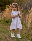 Toddler in Heyward House pima pink and white sleeveless dress in field.