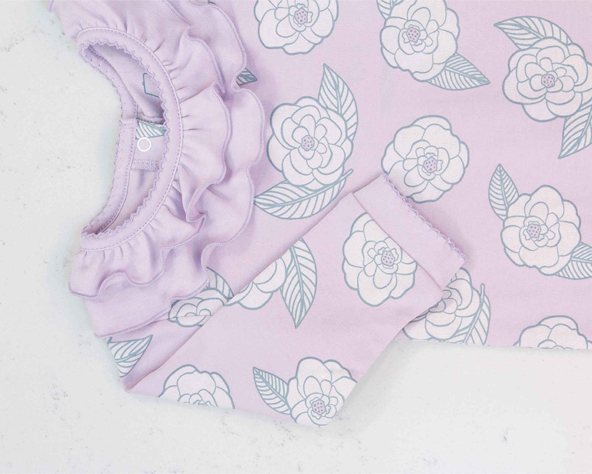 Close-up of pink girls playsuit with classic ruffled collar and camellia flower pattern made in pima cotton