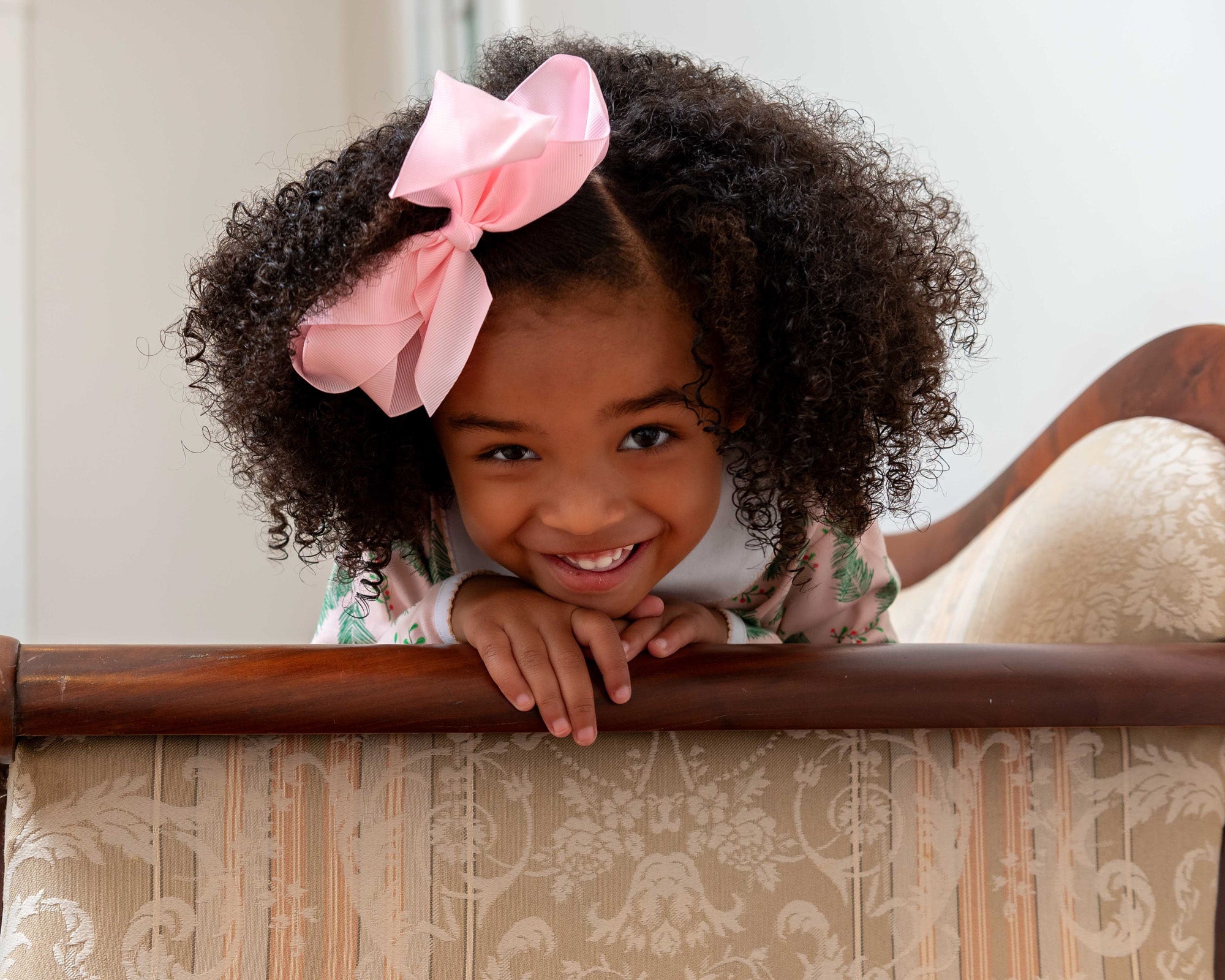 Little girl with big pink bow smiling wearing heyward house clothing