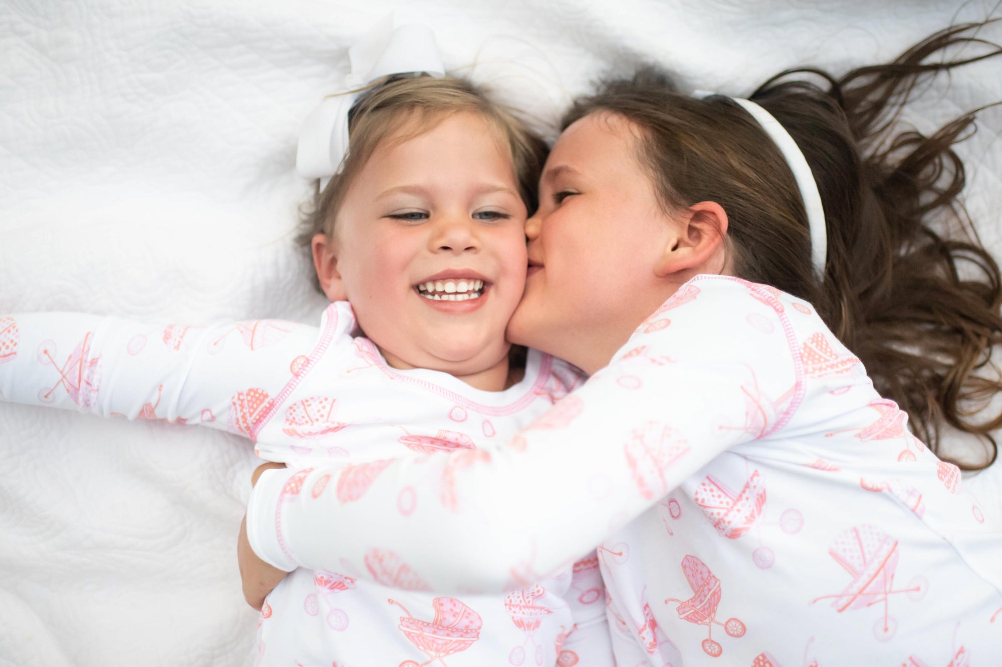 2 little girls kissing wearing pram pajamas by heyward house