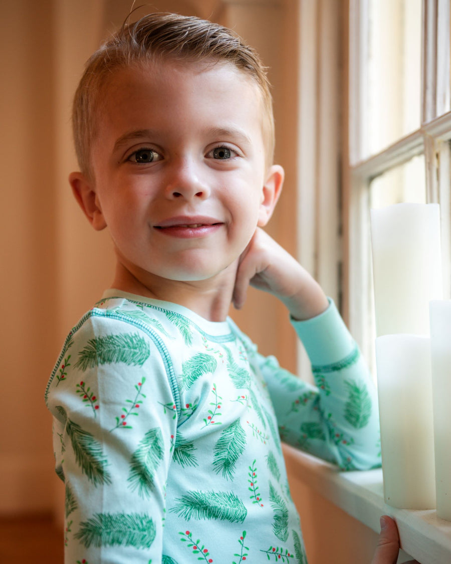 Little Boy wearing Blue two-piece pajama set with vintage Christmas holly pattern made with pima cotton