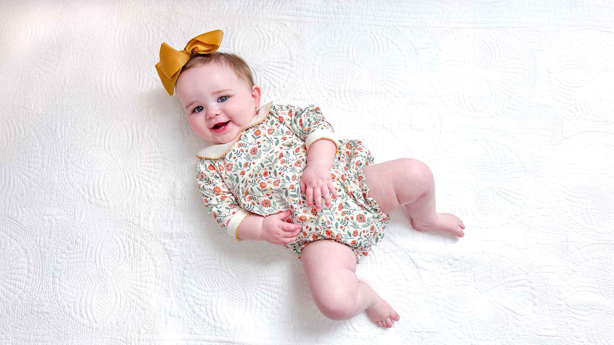 Baby wearing a floral bubbleand yellow bow on a white background