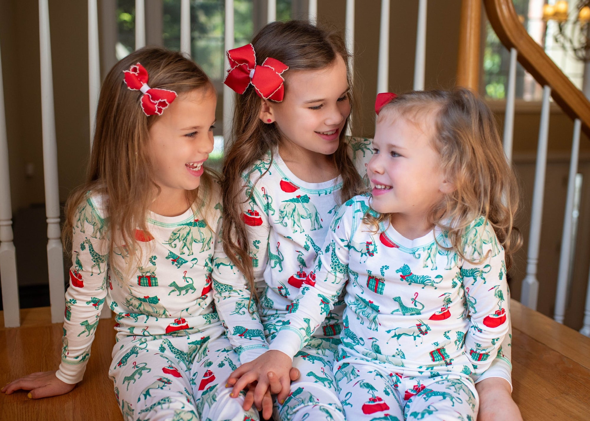 Three young girls wearing matching Christmas-themed pajamas sitting on a wooden floor.