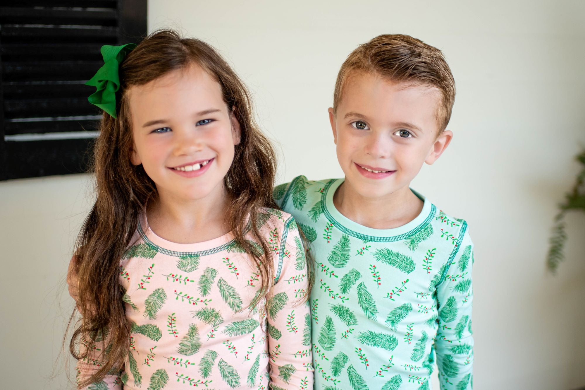 Children wearing Pink and Blue two-piece pajama sets with vintage Christmas holly pattern made with pima cotton