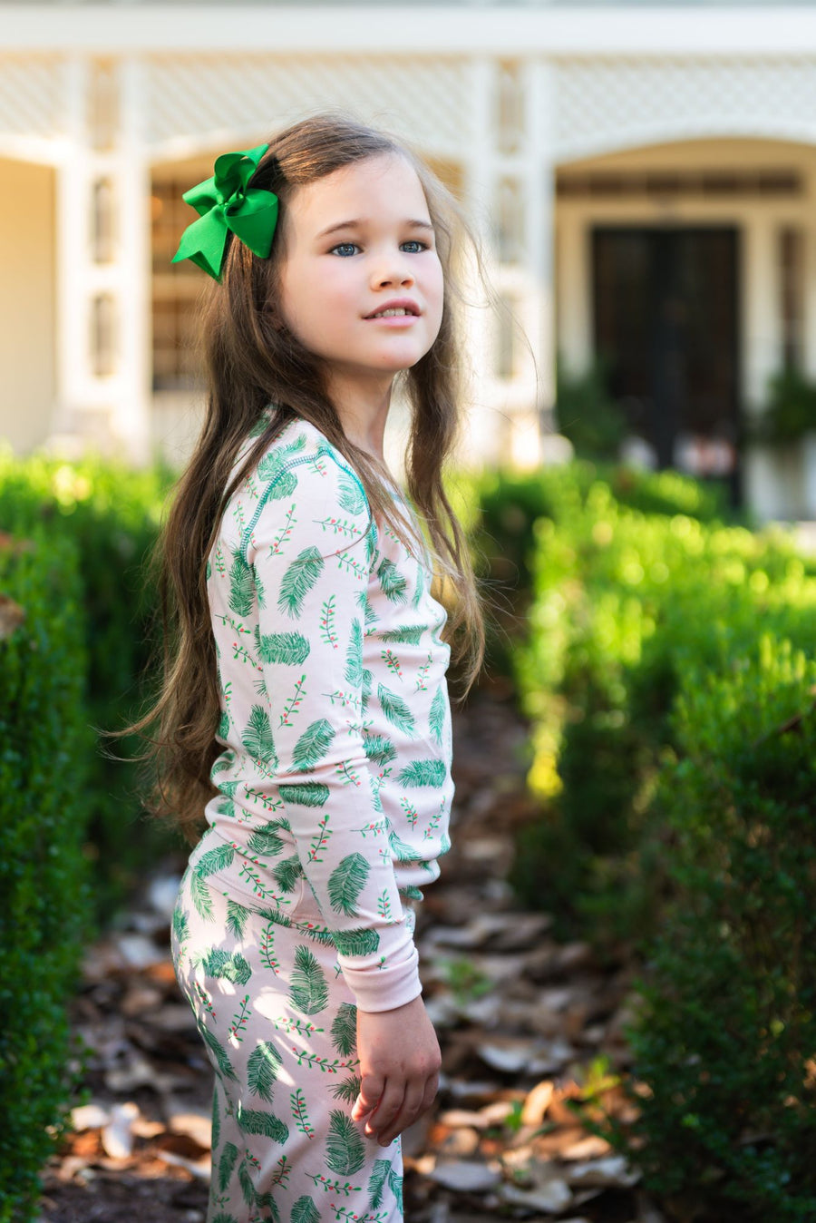 Little Girl wearing Pink two-piece pajama set with vintage Christmas holly pattern made with pima cotton