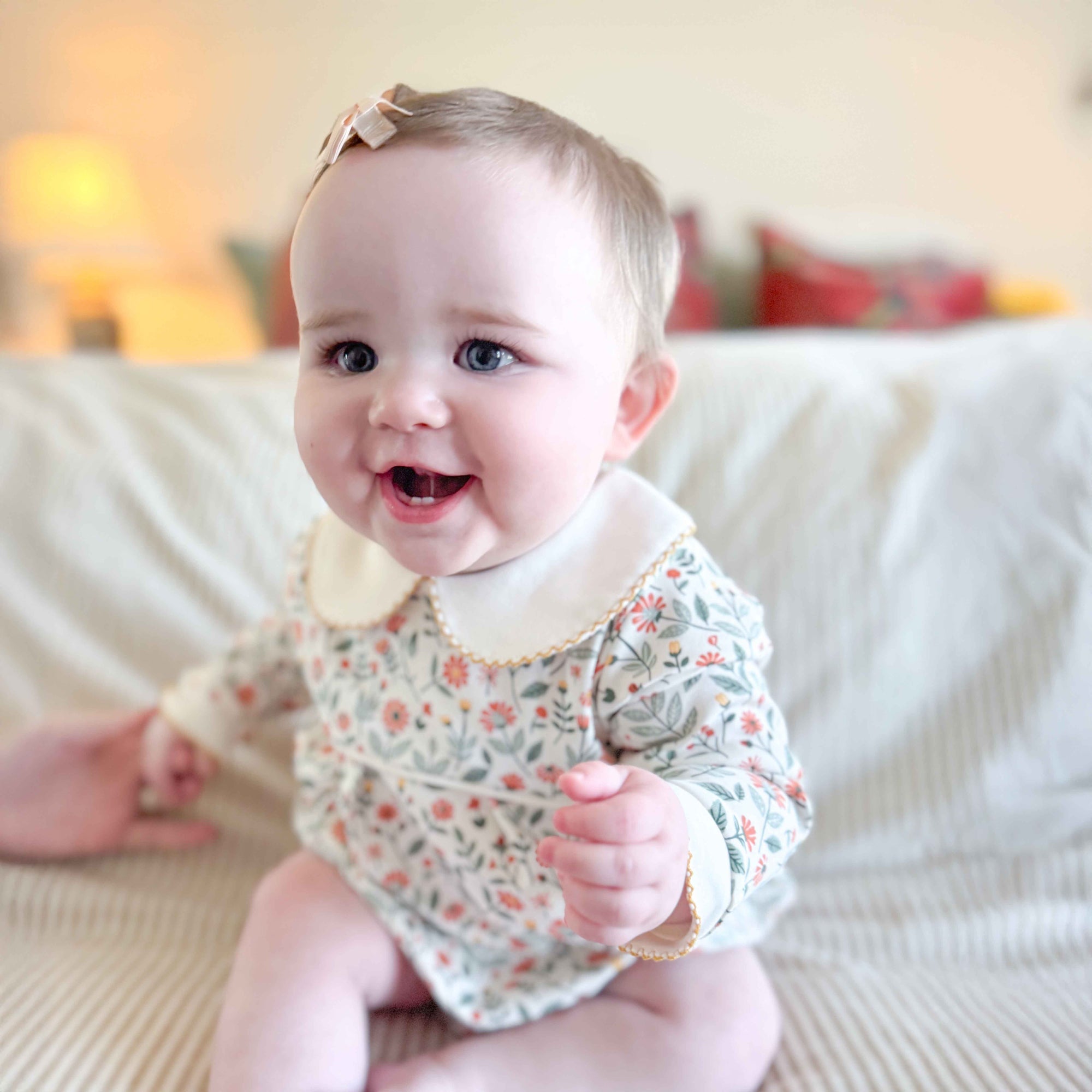 Baby wearing a floral onesie sitting on a couch