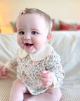Baby wearing a floral onesie sitting on a couch