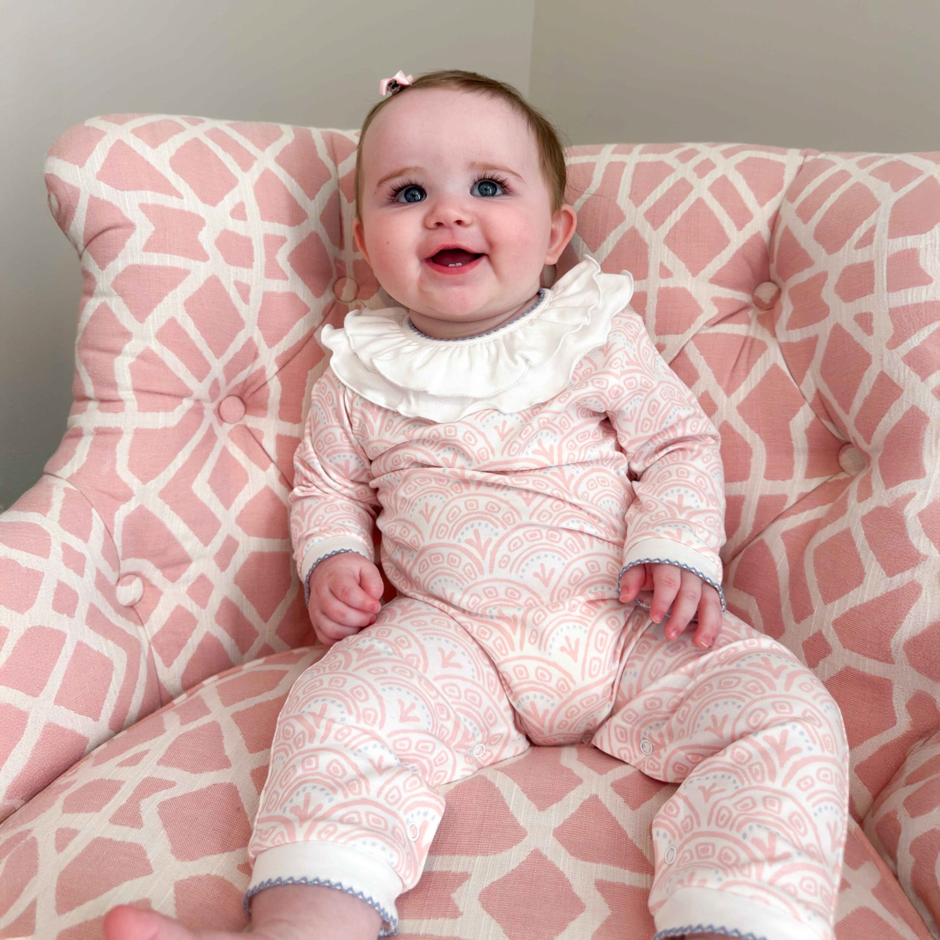 Baby in a pink and white patterned outfit sitting on a pink and white chair.
