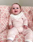 Baby in a pink and white patterned outfit sitting on a pink and white chair.