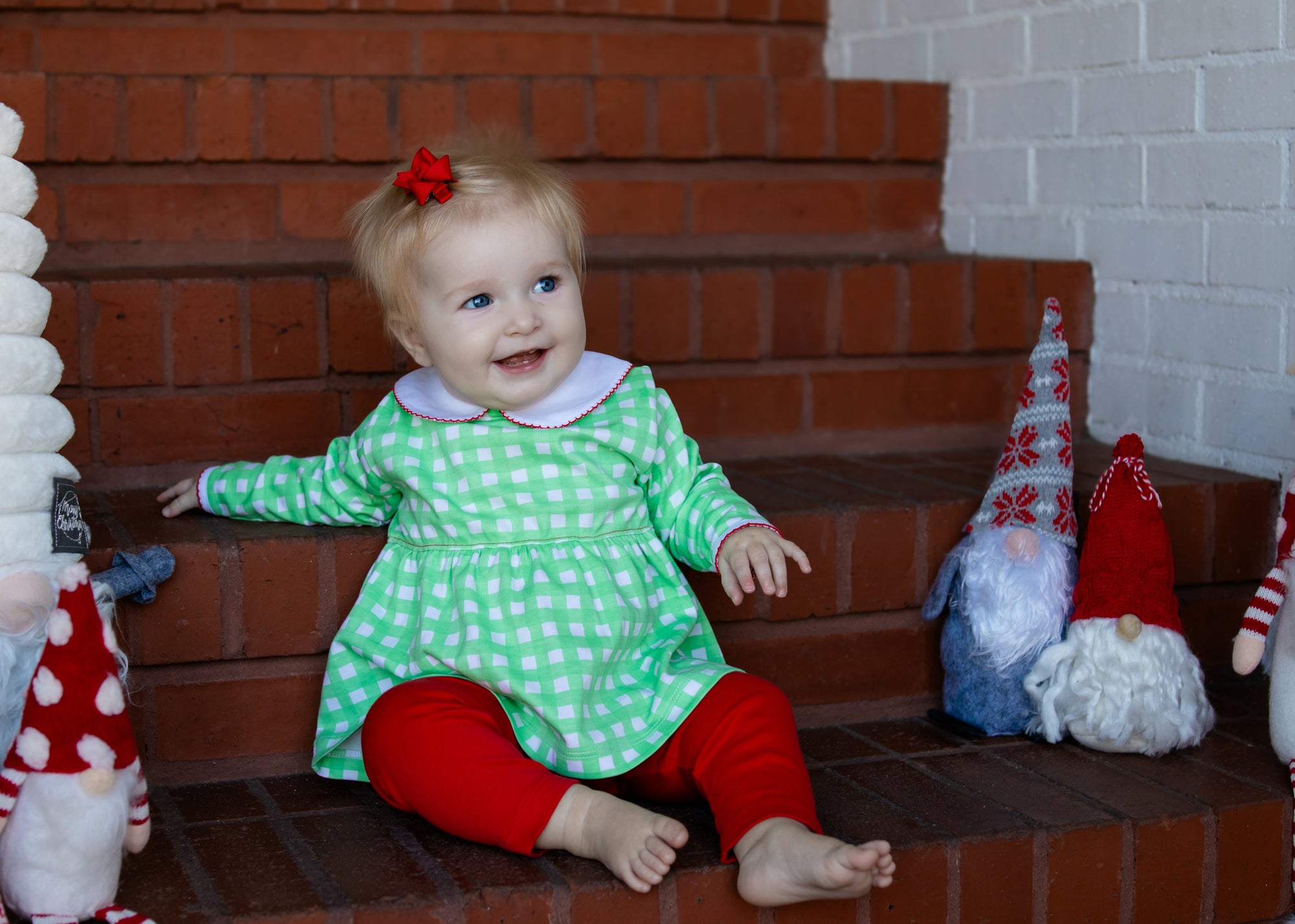 Child in a green dress with red accents sitting on a staircase surrounded by festive decorations.