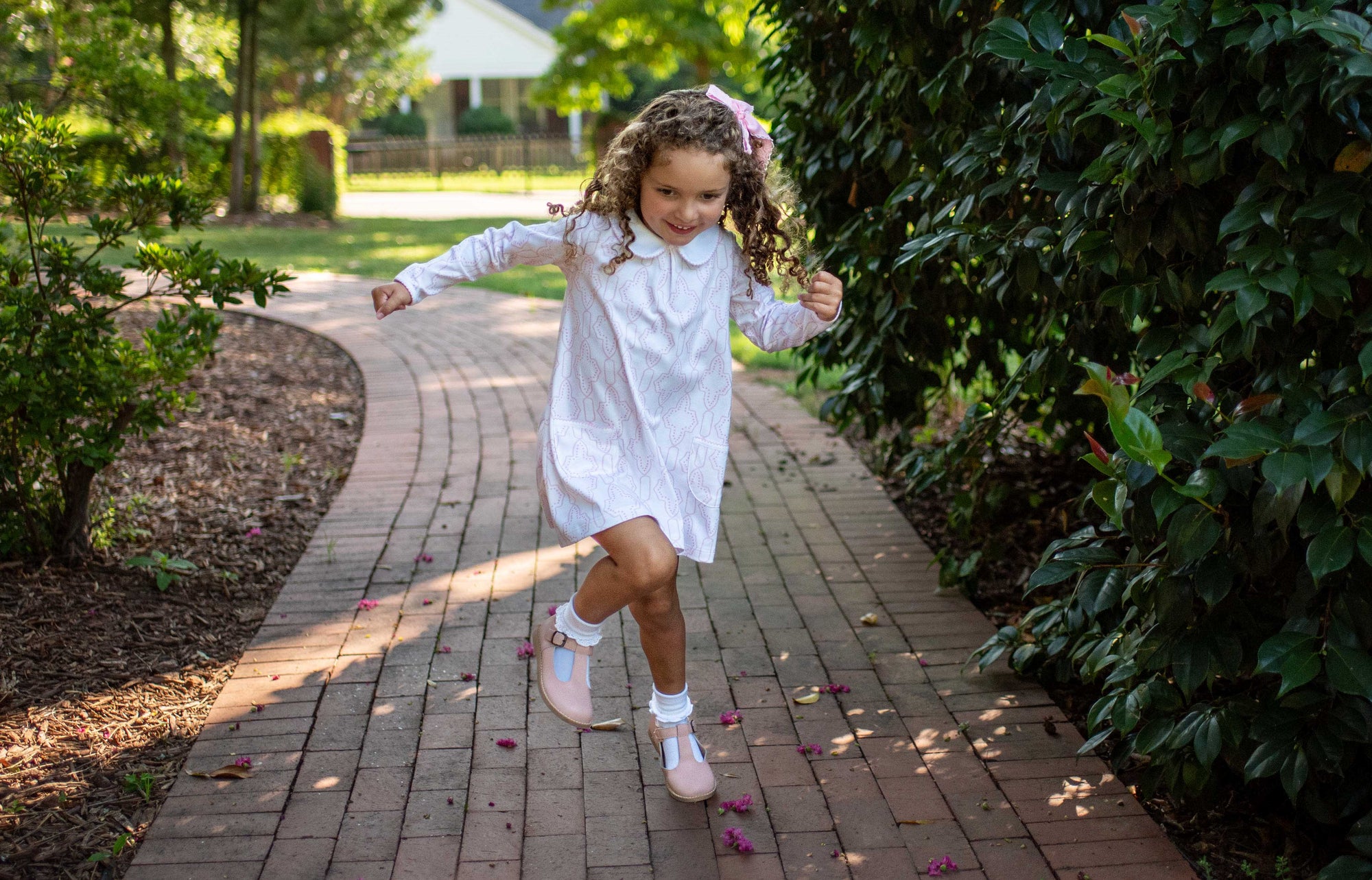 cute little girl smiling wearing heyward house twirl pocket dress. She is skipping down a brick sidewalk wearing soft pima cotton dress by heyward house.