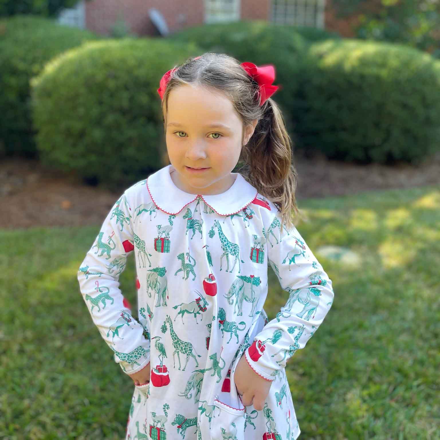 girl wearing safari christmas pocket dress in front of green bushes