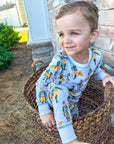 Child wearing pajamas with a fox pattern, sitting in a wicker basket outdoors.