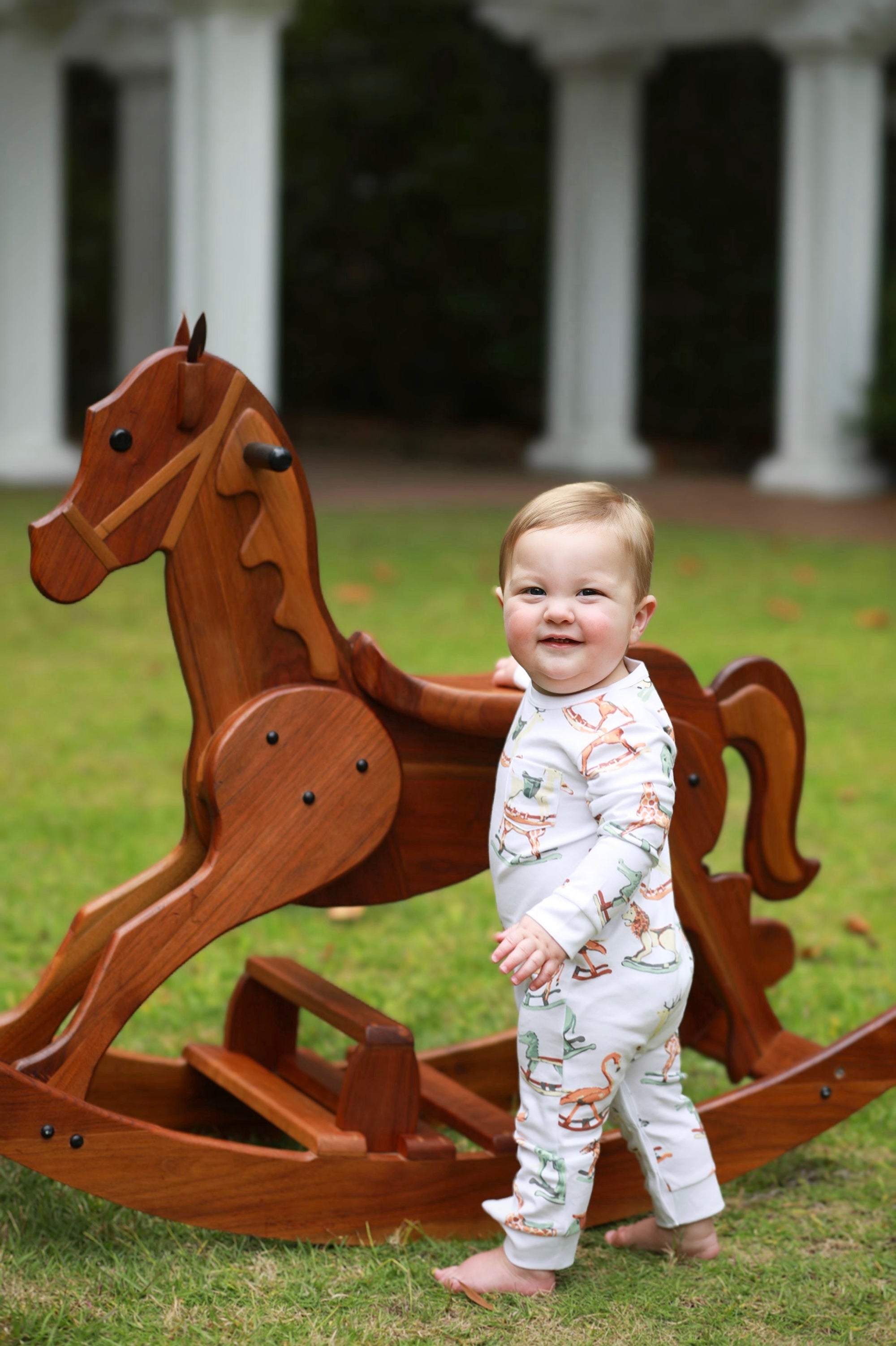 Child standing next to a wooden rocking horse in an outdoor setting