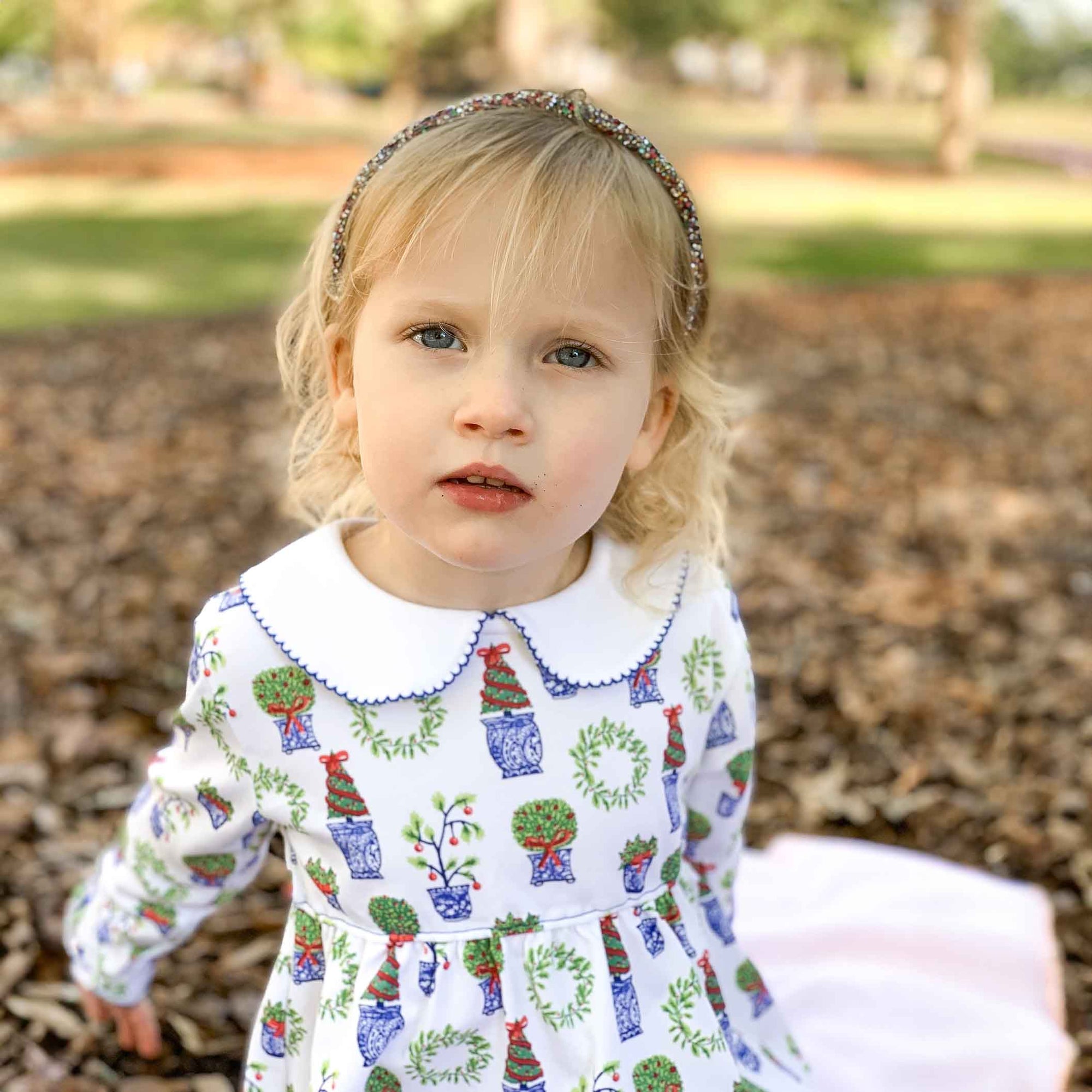 little girl with serious face wearing pima dress with holiday topiary print