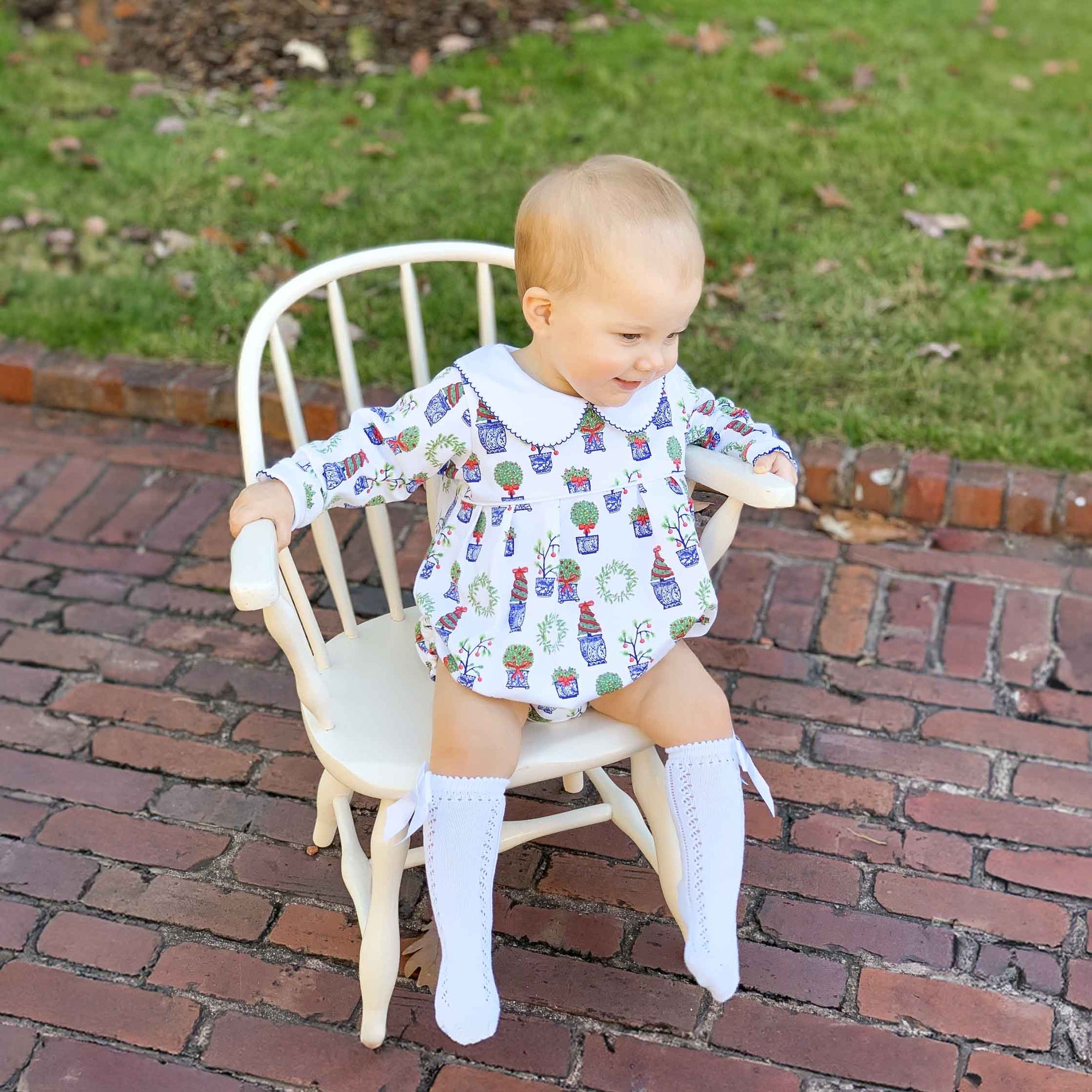 baby in chair wearing christmas bubble with knee socks and christmas plants design