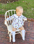 baby in chair wearing christmas bubble with knee socks and christmas plants design