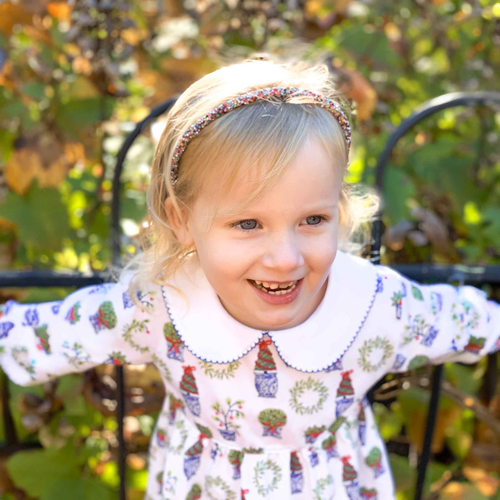 smiling little blonde girl wearing heyward house pima cotton dress leaning on fence