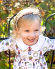 smiling little blonde girl wearing heyward house pima cotton dress leaning on fence