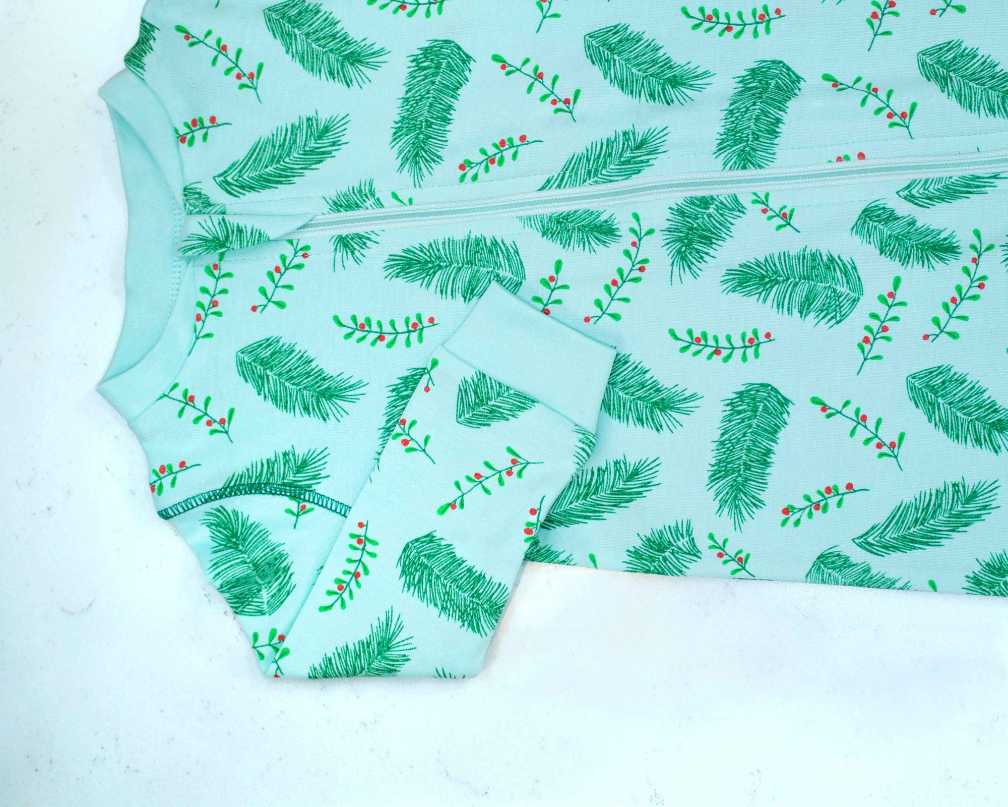 Detail of zipper area of light blue footed pajama with vintage Christmas holly pattern made in pima cotton