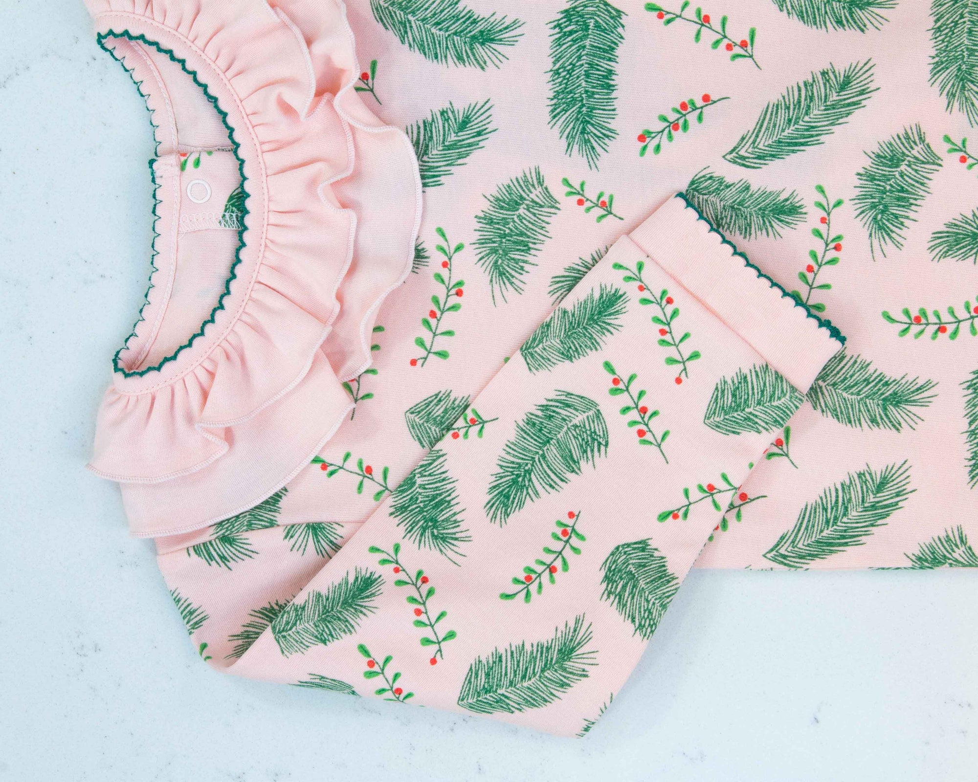 Close-up of pink girls playsuit with classic ruffled collar and vintage Christmas holly pattern made in pima cotton