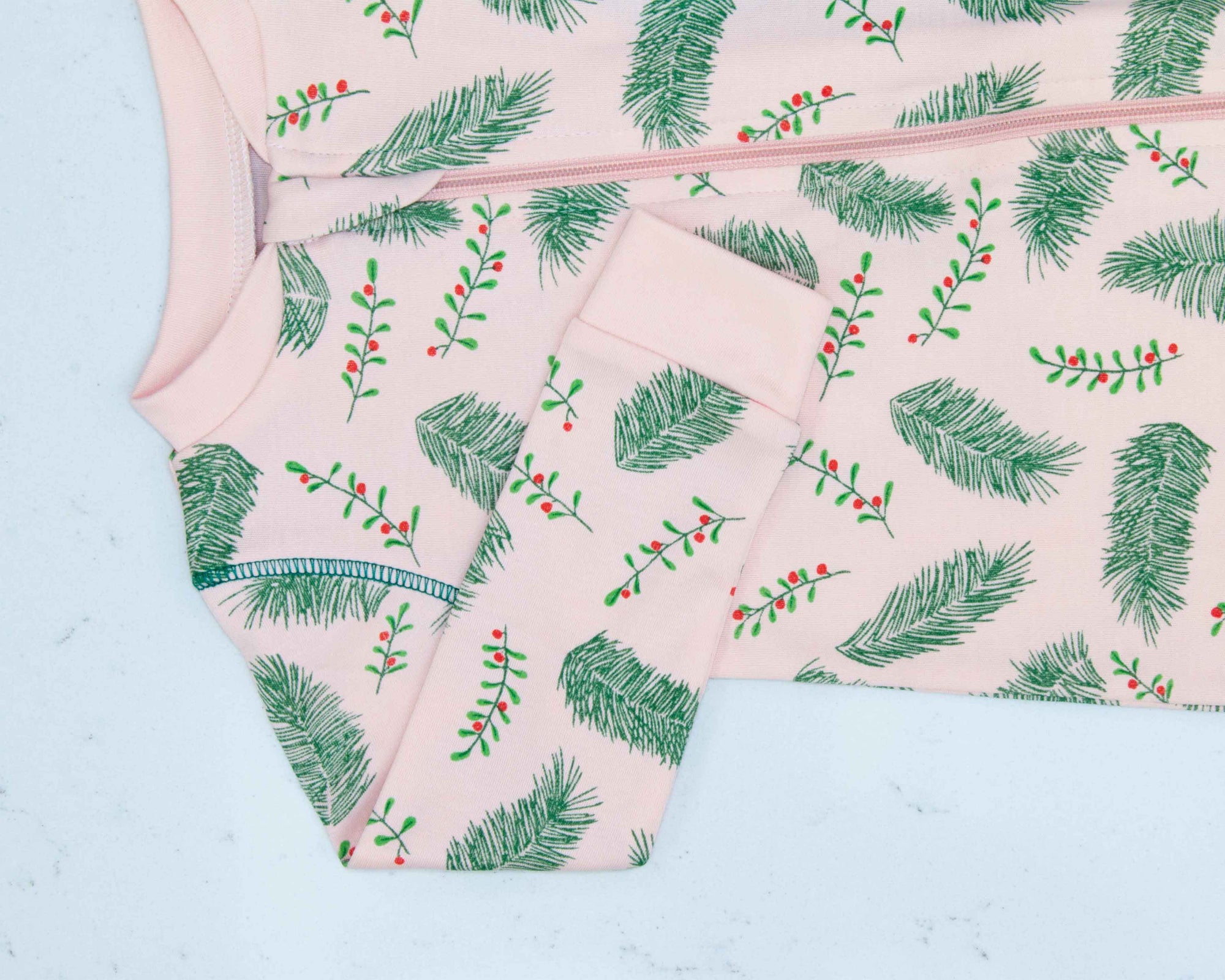 Detail of zipper area of light pink footed pajama with vintage-inspired Christmas holly pattern made in pima cotton