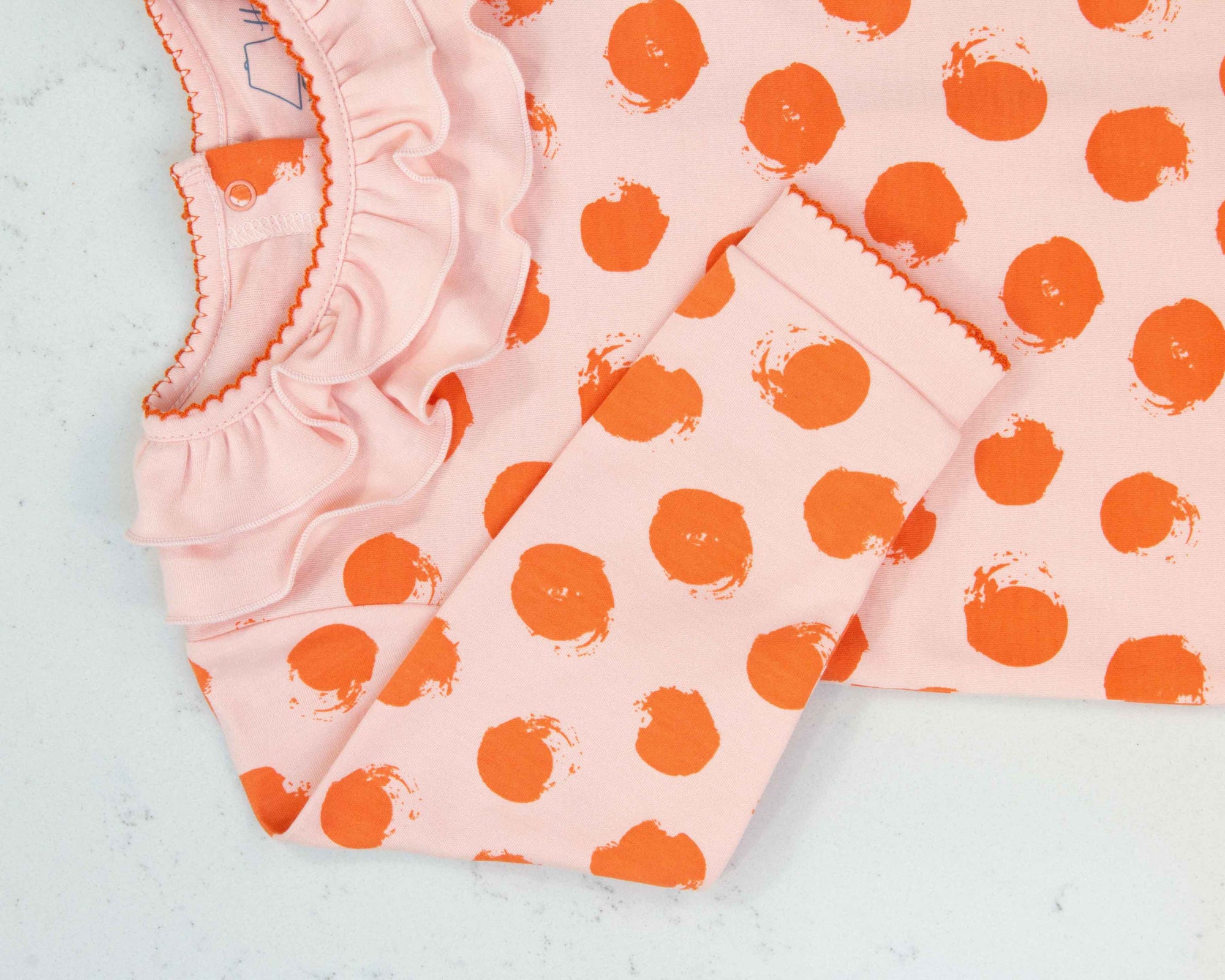 Close-up of pink girls playsuit with classic ruffled collar and orange dots pattern made in pima cotton