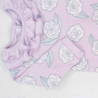 Close-up of pink girls playsuit with classic ruffled collar and camellia flower pattern made in pima cotton